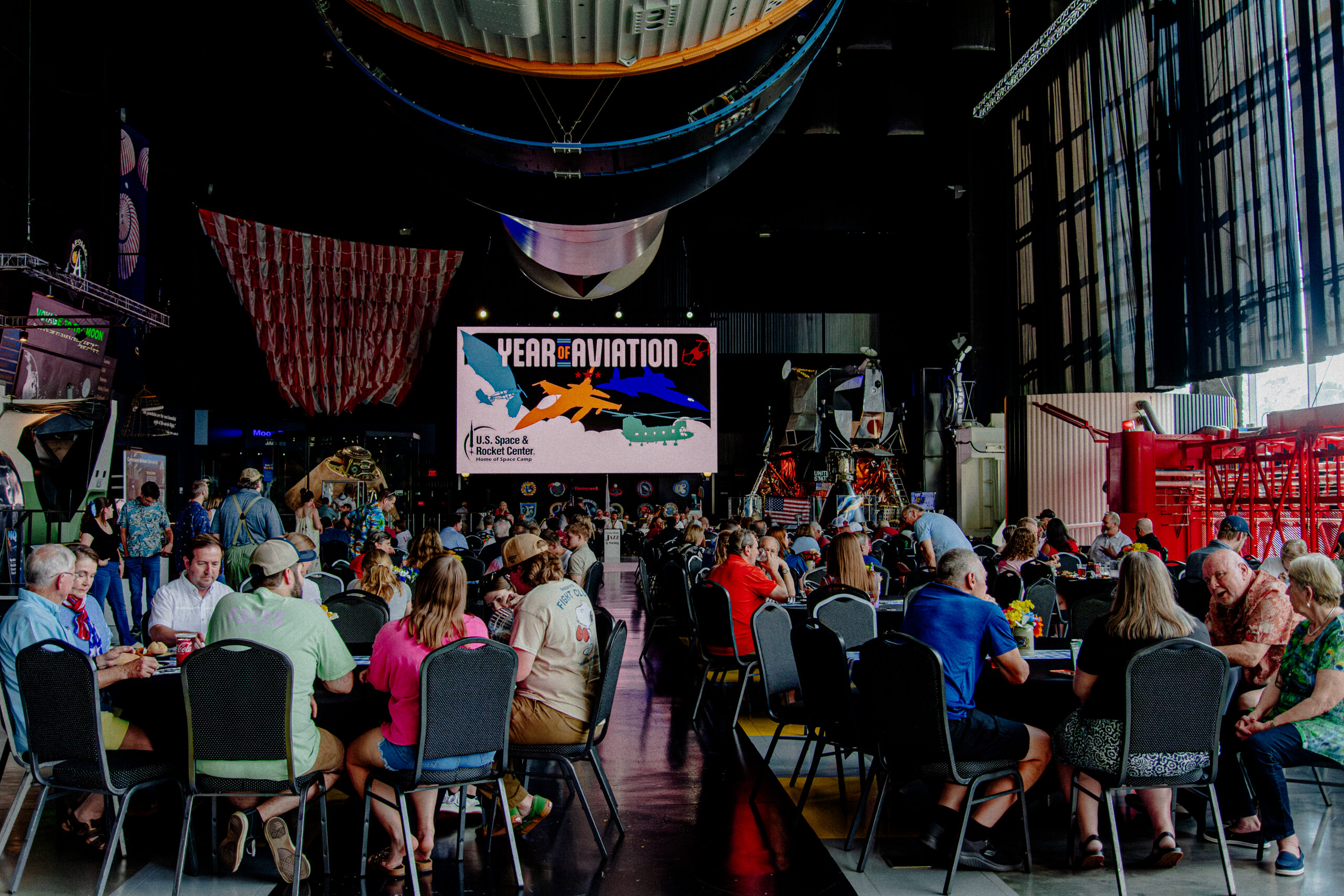 Group of individuals gathered for an event under the Saturn V rocket.