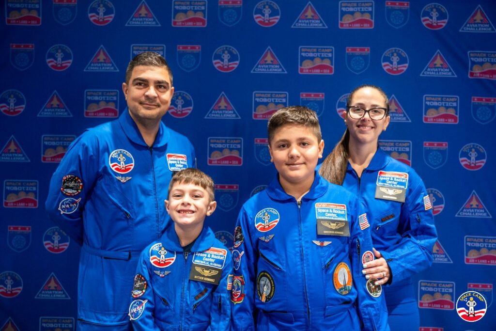 Family in blue Space Camp flight suits posing in front of a step-and-repeat backdrop