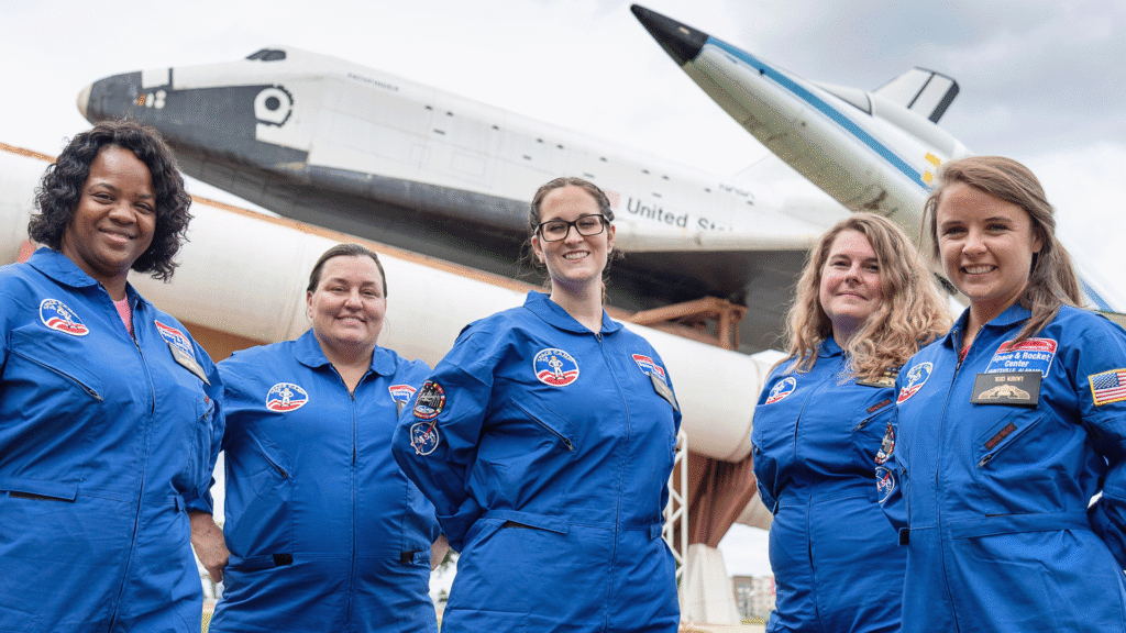 Group of adult trainees in blue flight suits in front of the space shuttle